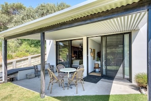 A covered outdoor patio with a table and chairs, a sliding glass door leading to a room, and a wooden deck.