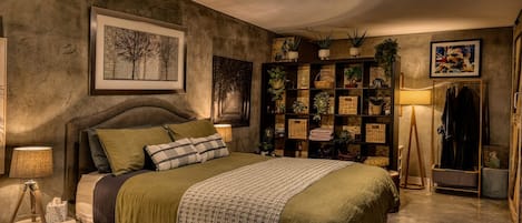 A bedroom with a bed, a ceiling fan, a wall-mounted shelf with plants, a framed picture, and a floor lamp.