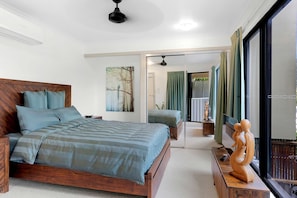 A bedroom with a wooden bed, a painting, a view of the outdoors, and a sculpture on a nightstand.