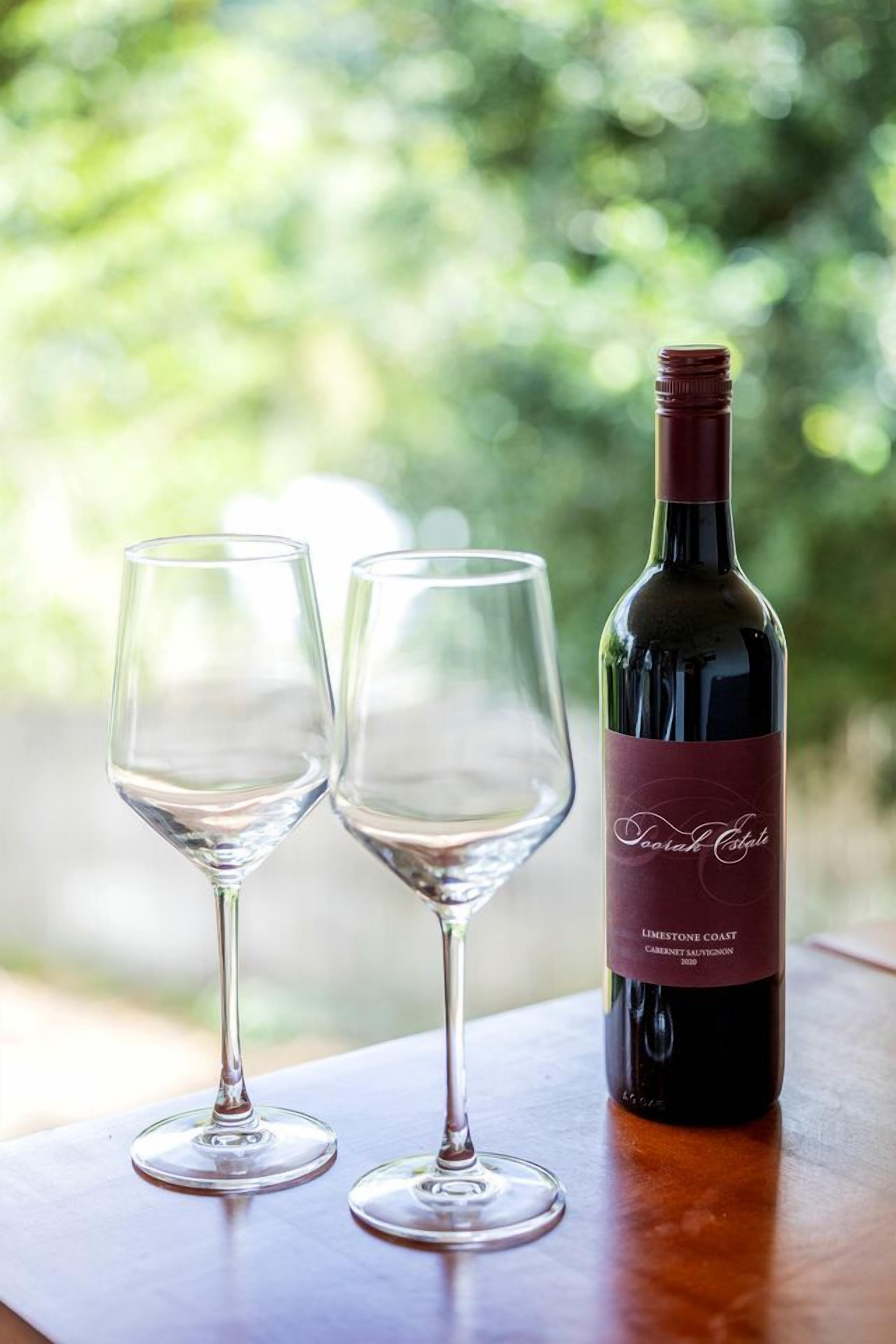 A wine bottle and two glasses on a wooden table with a blurred green background.