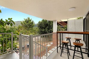 A balcony with a white railing, a wooden table, and three bar stools.