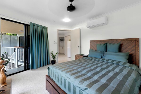 A bedroom with a bed, a nightstand, a potted plant, a sliding door to a balcony, and an air conditioning unit.