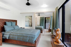 A bedroom with a wooden bed, a painting, a view of the outdoors, and a sculpture on a nightstand.