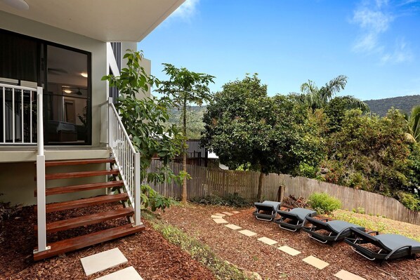 A modern house with a wooden deck, outdoor seating, and a view of a hilly landscape.