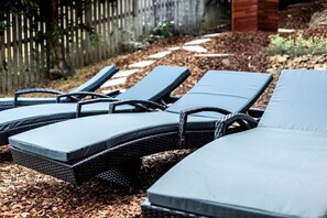 A row of outdoor lounge chairs with cushions, arranged on a wooden deck with mulch.