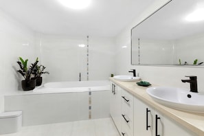 Ein modernes Badezimmer mit Badewanne, zwei Waschbecken, Toilette und Topfpflanzen.