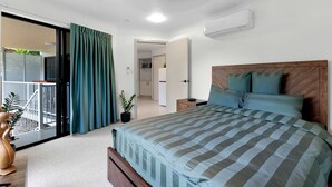 A bedroom with a bed, a nightstand, a potted plant, a sliding door to a balcony, and an air conditioning unit.