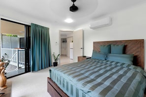 A bedroom with a bed, a nightstand, a potted plant, a sliding door to a balcony, and an air conditioning unit.