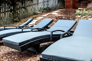 Eine Reihe von Liegestühlen mit Kissen, auf einer Holzterrasse mit Mulch angeordnet.