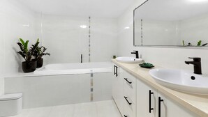 A modern bathroom with a bathtub, two sinks, a toilet, and potted plants.