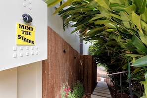 A building exterior with a 'MIND THE STAIRS' sign, a wooden fence, and a staircase leading to a garden area.