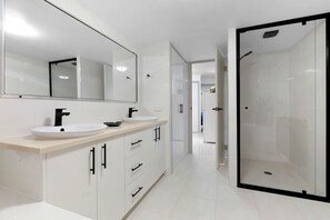 A modern bathroom with two sinks, a large mirror, and a walk-in shower.