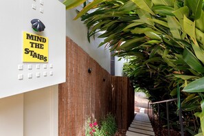 Ein Gebäude mit einer Außenansicht, einem Schild mit der Aufschrift 'MIND THE STAIRS', einem Holzzaun und einer Treppe, die zu einem Garten führt.