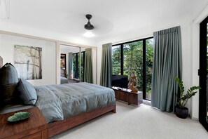 A bedroom with a bed, TV, and a view of greenery outside.