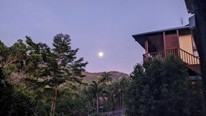 A building with a balcony overlooking a forested area and a hill in the background.