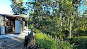 A modern building with an open kitchen and dining area, surrounded by a forest. - Off-Grid Equipped Container with Outdoor Pool and Amazing Views in Queensland (Gold Coast)