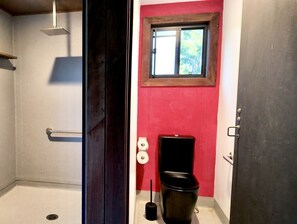 A bathroom with a shower, toilet, and window.