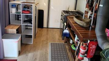 Een kleine keuken met een inbouwfornuis, een koelkastje en een houten plank met keukengerei.
