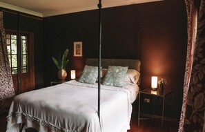 Ein Schlafzimmer mit einem Himmelbett, einem Nachttisch mit Lampe, einem Blumentopf und einem gerahmten Bild an der Wand.