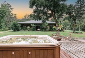 Ein Whirlpool auf einer Holzterrasse mit einer Rasenfläche und einem Haus im Hintergrund.