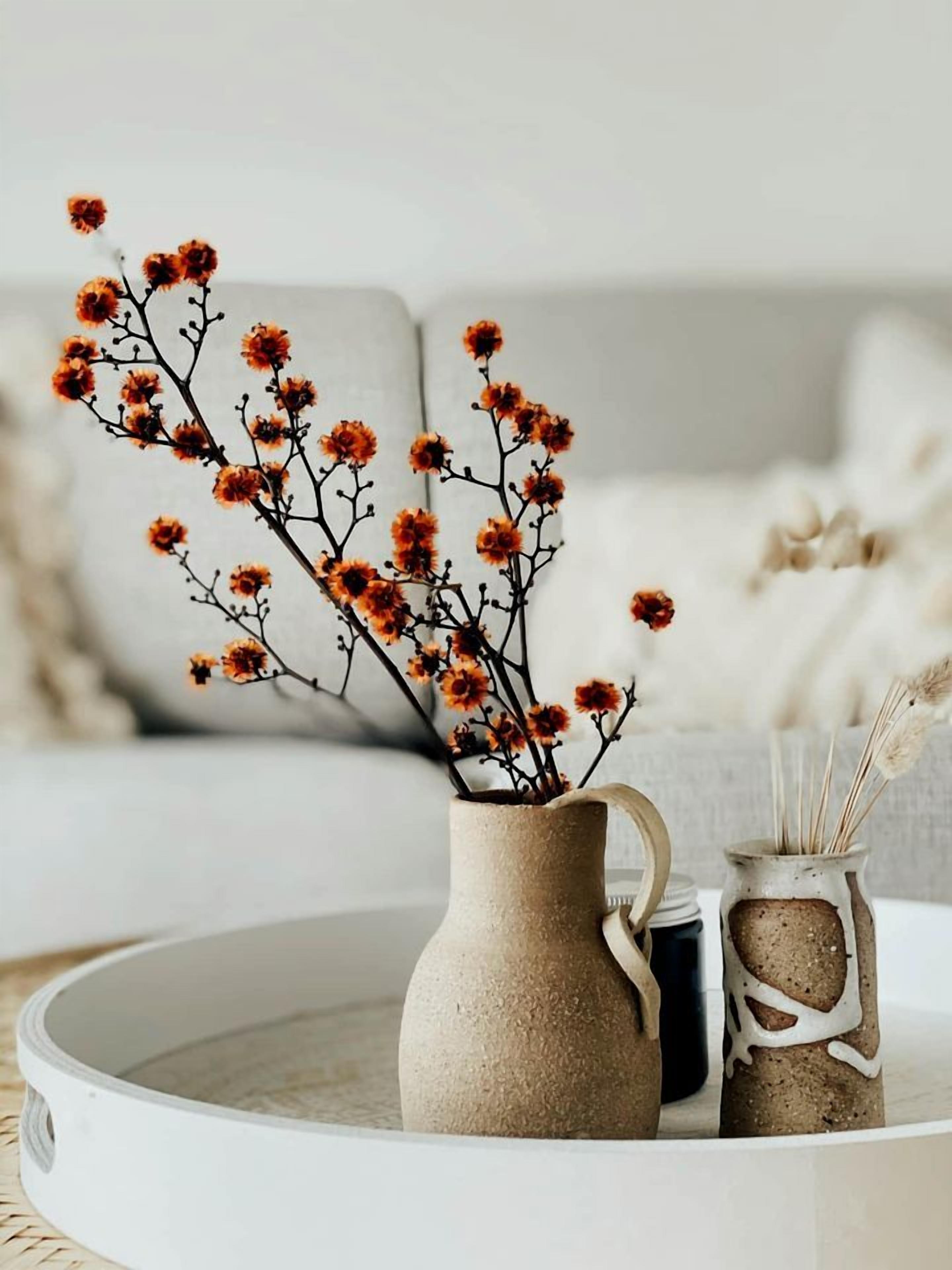 A beige ceramic vase with branches and small orange flowers on a white tray.