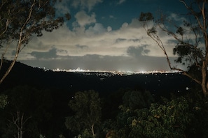 Vista nocturna de un paisaje urbano con edificios iluminados bajo un cielo nublado, rodeado de árboles.
