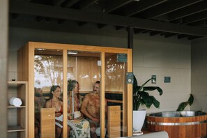 Un sauna aux murs en bois et Ă la porte en verre, avec un banc en bois et une grande plante en pot.