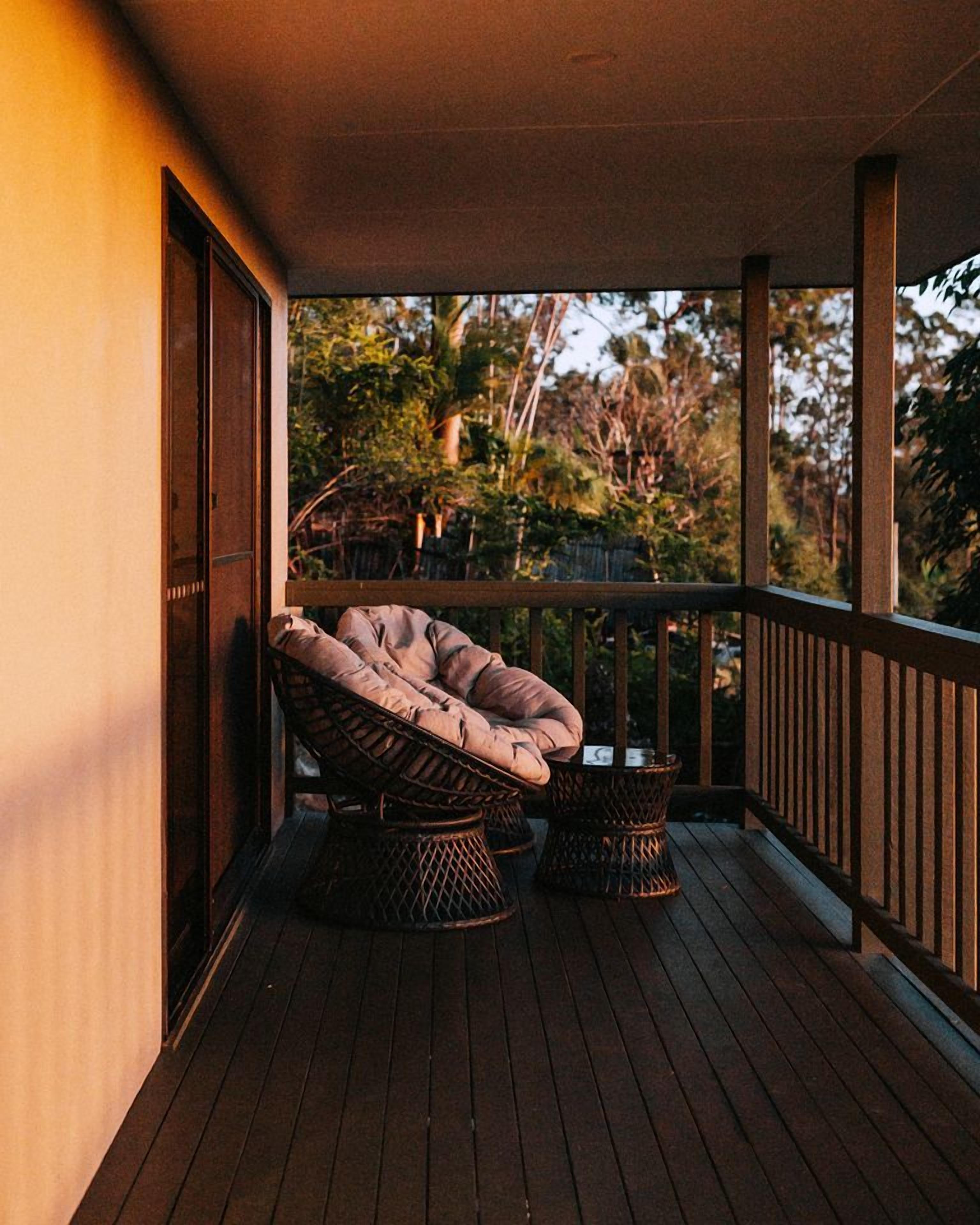 Une terrasse en bois avec une chaise en osier et une petite table, le tout entouré d’une balustrade en bois.