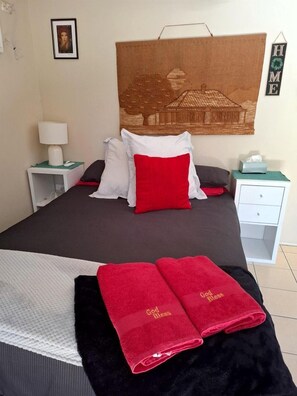 A neatly made bed with a headboard, a bedside table with a lamp, a framed picture on the wall, and a 'HOME' sign.