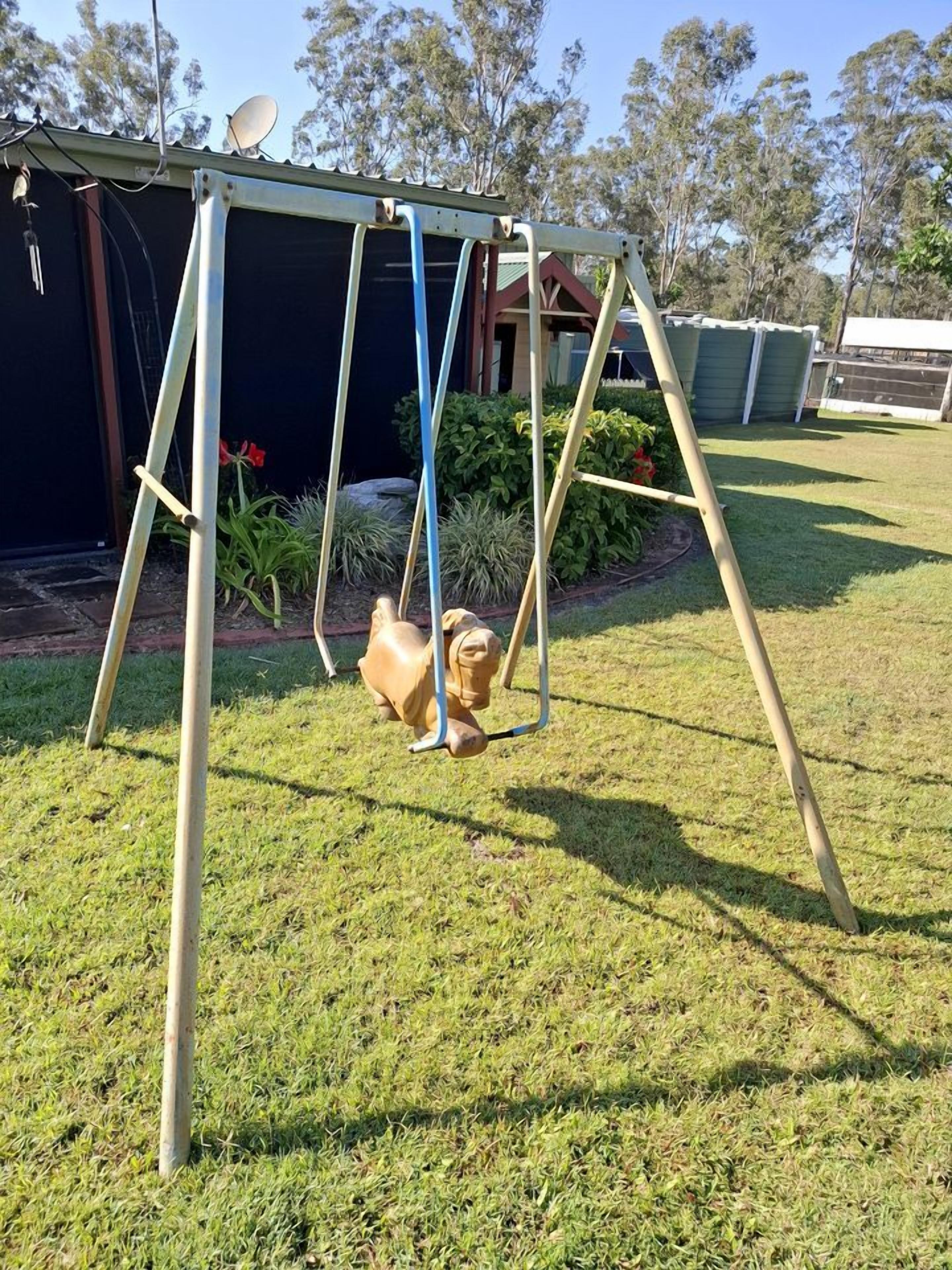 A swing set in a grassy yard with a house in the background.