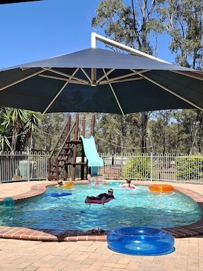 Una piscina con tobogán, flotadores y una zona cubierta.