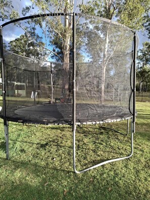 A trampoline with a safety net, surrounded by grass and trees.