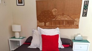 Una cama bien hecha con cabecera, una mesita de noche con lámpara, un cuadro en la pared y un cartel que dice 'HOME'.