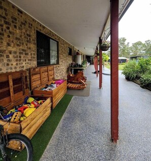 Un espacio al aire libre techado con bancos de madera, una bicicleta y una zona de juegos con juguetes.