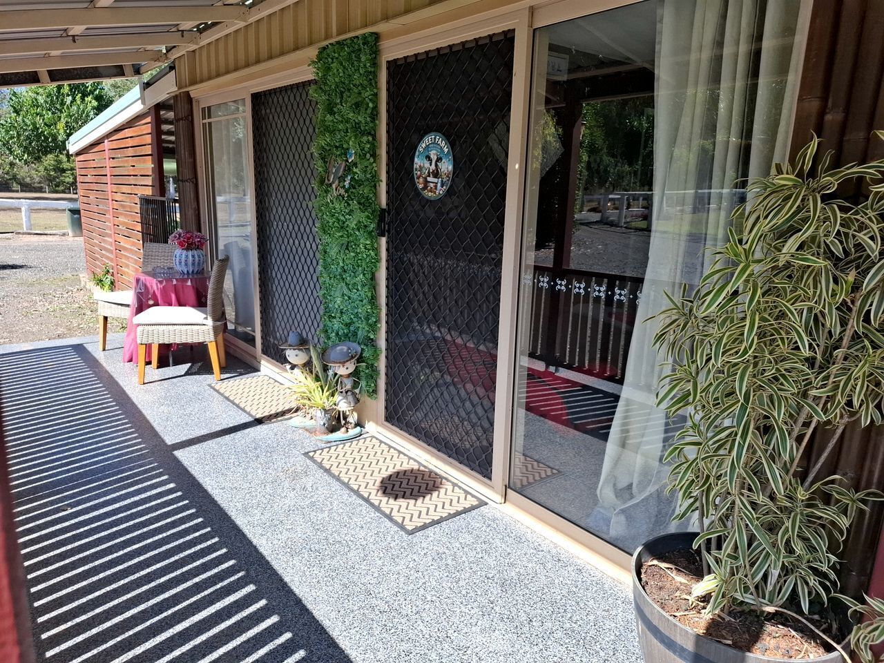 A covered outdoor seating area with a table and chairs, a potted plant, and a door with a security screen.