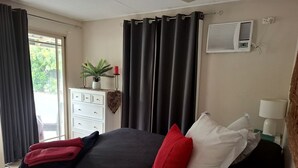 Een slaapkamer met een bed, een kaptafel, een bloempot, gordijnen en een airconditioning.