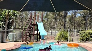 Una piscina con tobogán, flotadores y una zona cubierta.