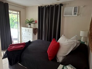 Un dormitorio con cama, cómoda, planta en maceta, cortinas y equipo de aire acondicionado.
