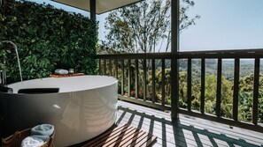 Un espace spa comprenant un bain à remous, une terrasse en bois et une vue sur la forêt environnante.
