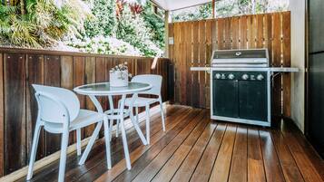 An outdoor patio with a wooden deck, a round table with white chairs, and a built-in grill.