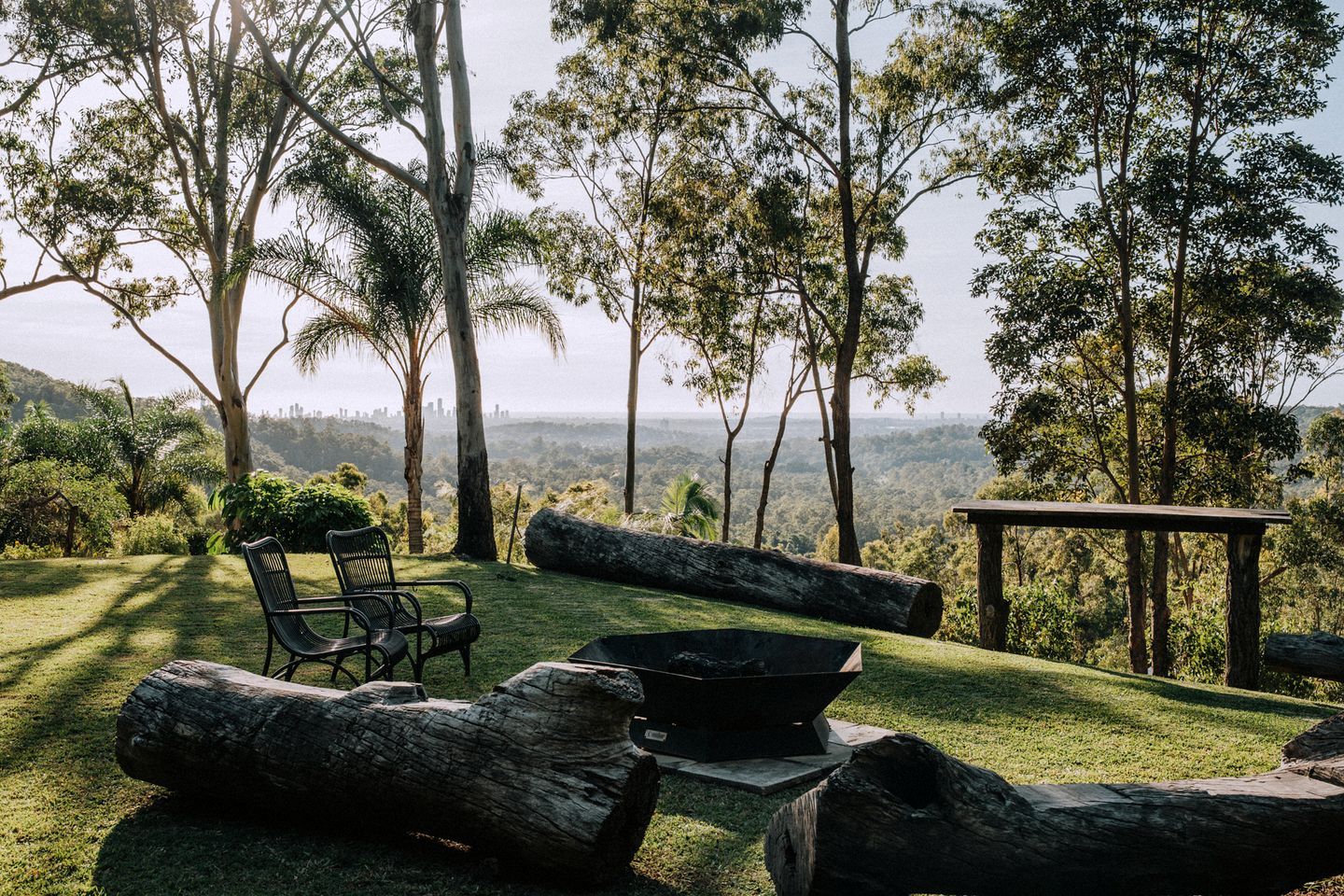 A grassy outdoor area with a fire pit, two chairs, and a wooden table.