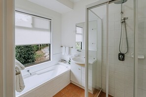 Ein modernes Badezimmer mit einer Badewanne, einer Dusche, einem Waschbecken und einem Fenster mit Blick auf Grünflächen.
