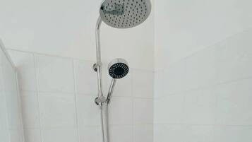 Une douche équipée d’un pommeau de douche à main et d’un pommeau de douche mural, dans une salle de bain aux murs recouverts de carreaux blancs.