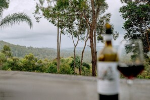 Una botella de vino y una copa sobre una mesa con vistas a árboles y colinas.
