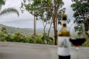 A bottle of wine and a glass on a table with a view of trees and hills.