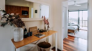 A bedroom with a bed, a wooden desk with a mirror, a welcome sign, and a view of a balcony.