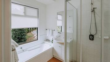 A modern bathroom with a bathtub, a shower, a sink, and a window with a view of greenery.