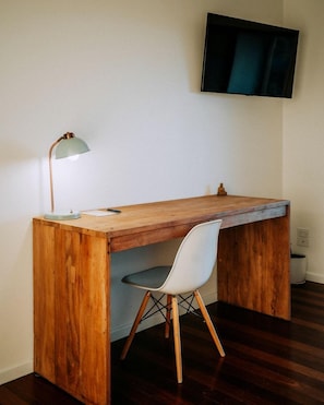 Uma mesa de madeira com uma cadeira, uma luminária e uma televisão fixada na parede.