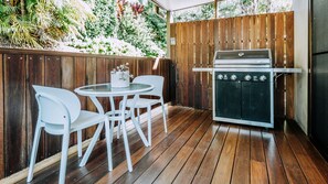 Eine Terrasse im Freien mit Holzdeck, einem runden Tisch und weißen Stühlen sowie einem eingebauten Grill.