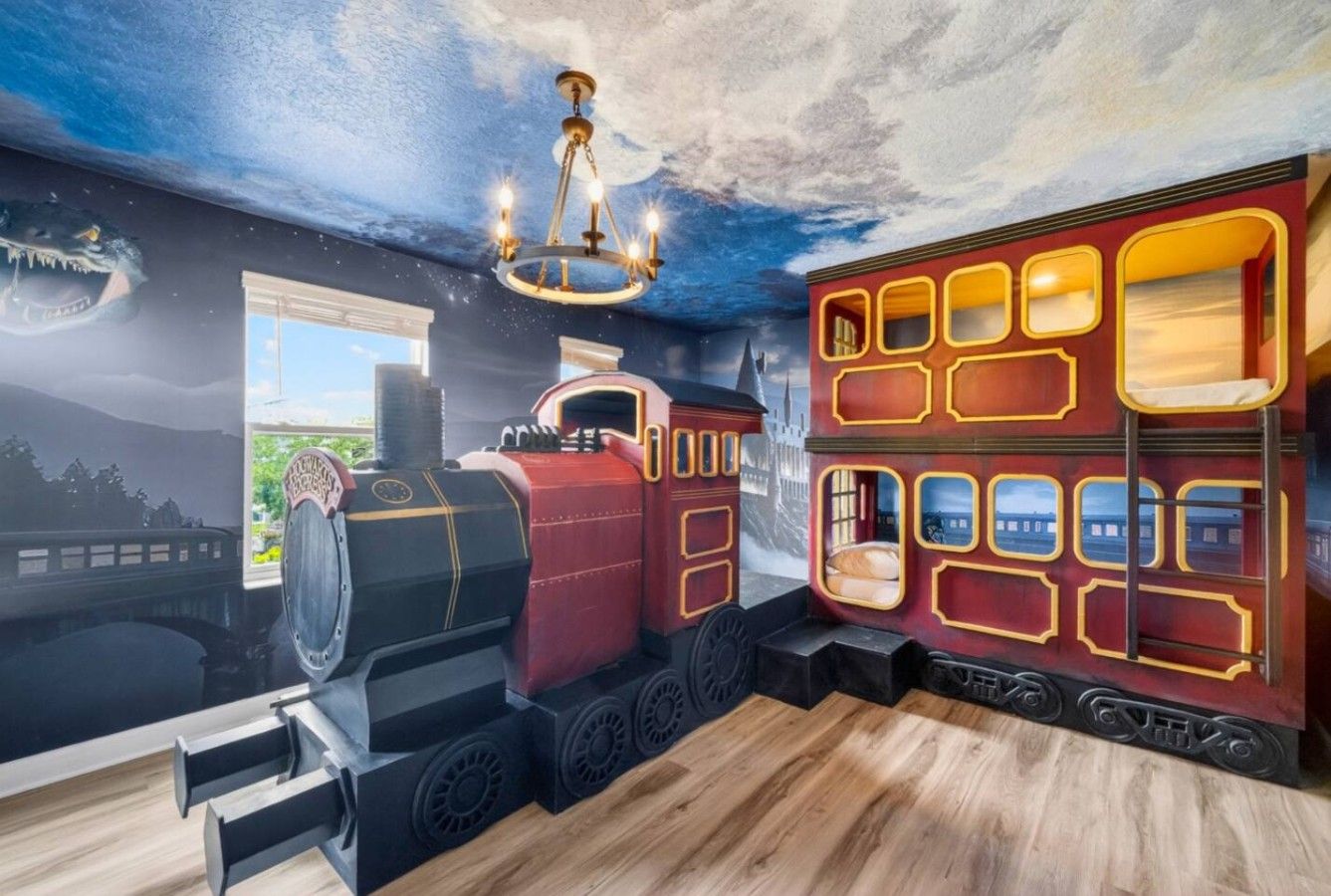 A room with a mural of a train, a chandelier, and a window with a view of a cityscape.